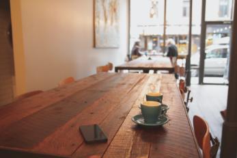 Coffee cups and phone on wooden table in a cafe